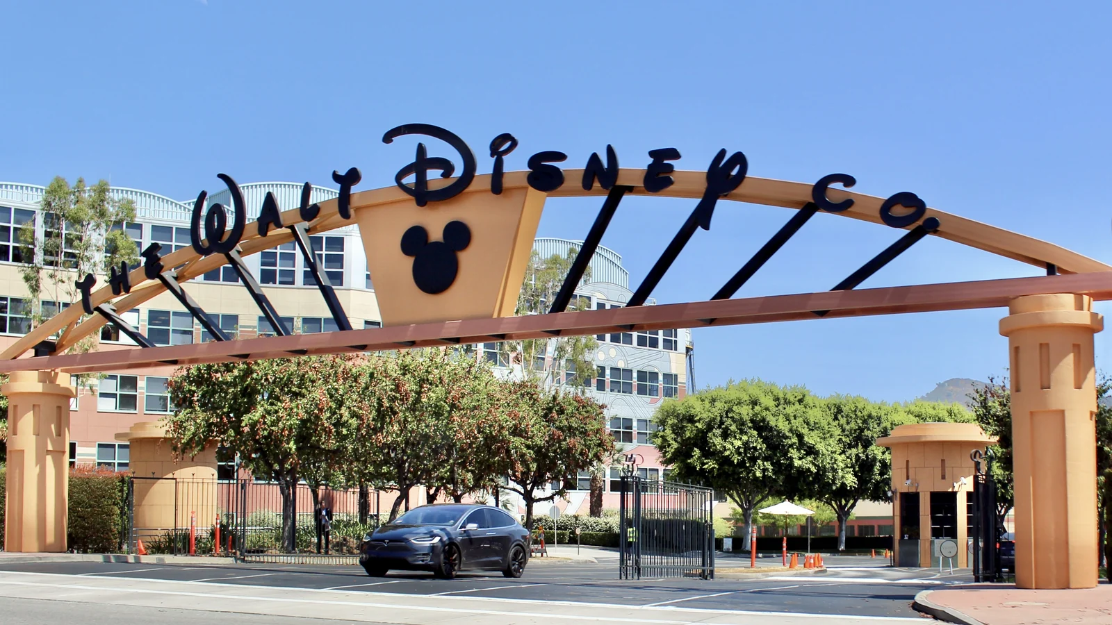 A large peach-colored entrance gateway with an arched metal frame and black stylized lettering reading “WALT DISNEY CO…” is visible.