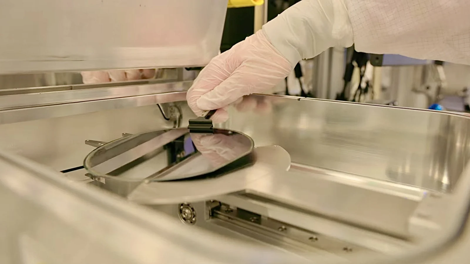 Screenshot from a Creative Commons-licensed YouTube video showing a worker removing a semiconductor wafer from semiconductor manufacturing equipment.